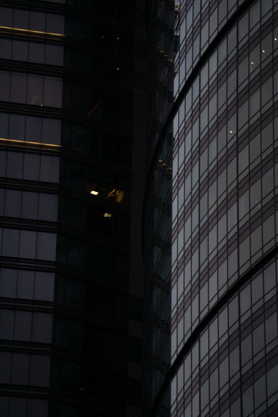 Fachada de vidrio de una torre corporativa con una oficina encendida